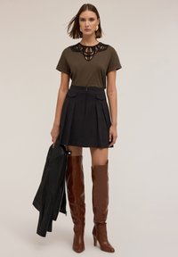 Hnědé kožené nadkolenky, černá plisovaná sukně, olivově zelený top s černou krajkou u výstřihu a černá kožená bunda.