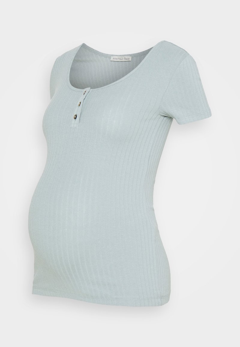 Jasnoniebieska, prążkowana, krótko rękawowa bluzka ciążowa z dekoltem henley na trzy guziki i dopasowanym krojem na białym tle.