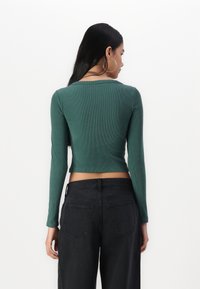 Grønn ribbete langermet topp med et Cropped-design, kombinert med høyt liv svarte jeans med baklommer og minimal søm.