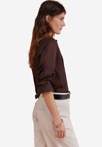 Bruine overhemd met opgerolde mouwen, gecombineerd met crémekleurige textuurbroek en een zwarte riem. Eenvoudig ontwerp met een losse fit.