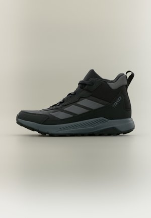 Μαύρο και γκρι ορειβατικό παπούτσι Adidas Terrex με μεσαίο επάνω μέρος, επενδεδυμένο περιλαίμιο, κλείσιμο με κορδόνια και ανθεκτική σόλα για εξωτερική χρήση.