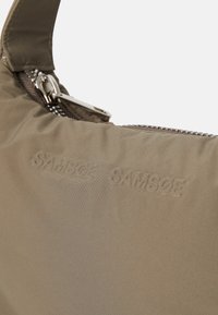 Geantă khaki dintr-un material texturat, cu închidere cu fermoar și logo-ul „SAMSØE” debossat. Suprafață netedă și design rotund. Accente din metal argintiu.