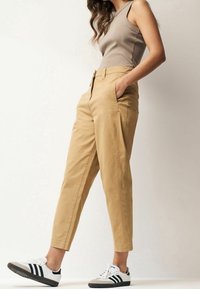 Beżowe bawełniane chinosy z tapered legs, z bocznymi kieszeniami i zamkiem błyskawicznym. Połączone z czarno-białymi trampkami z trzema paskami.