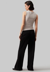 Getailleerde lichtgrijze mouwloze top gecombineerd met wijde zwarte broek. Smoothe stof met minimale details en een gestroomlijnd silhouet.