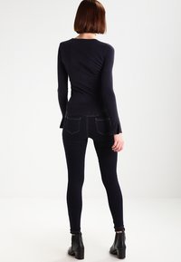 Haut en maille côtelée bleu marine avec manches longues et poignets évasés, associé à un jean skinny foncé et des bottines, vu de dos.