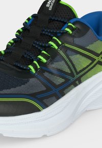 Chaussure de course noire et vert néon avec des accents bleus, empeigne en mesh, lacets à motifs et semelle blanche épaisse texturée.