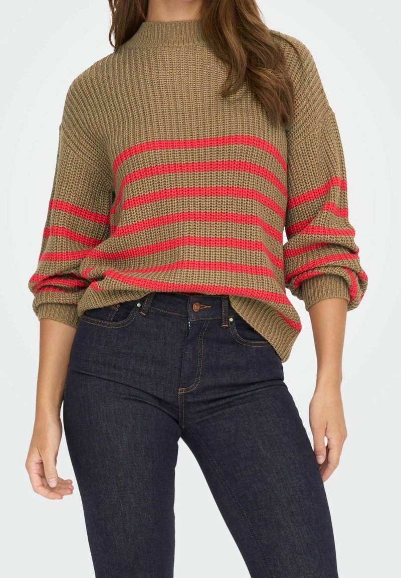Suéter de punto en beige con rayas horizontales rojas, que presenta un cuello alto y mangas sueltas. Combinado con jeans azul oscuro.
