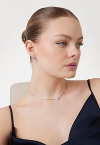 Collana d'argento con pendente circolare caratterizzato da una pietra preziosa, abbinata a orecchini a bottone coordinati. Superficie liscia e lucida; design elegante.