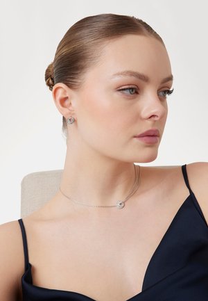 Collana d'argento con pendente circolare caratterizzato da una pietra preziosa, abbinata a orecchini a bottone coordinati. Superficie liscia e lucida; design elegante.