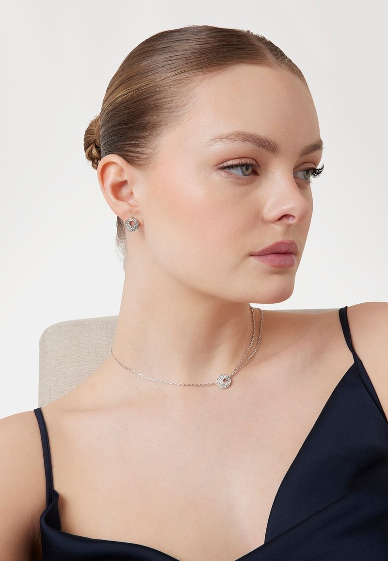 Collana d'argento con pendente circolare caratterizzato da una pietra preziosa, abbinata a orecchini a bottone coordinati. Superficie liscia e lucida; design elegante.