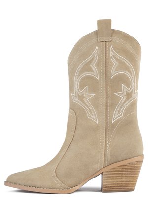 Botte de cow-boy en daim beige avec un bout pointu, des coutures blanches décoratives et un talon en bois empilé. Elle présente une languette à l'arrière.