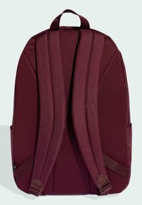 Zaino in tessuto bordeaux con una consistenza texturizzata, dotato di spallacci imbottiti, maniglia superiore e tasche laterali. Design minimalista.