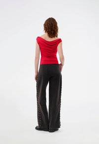 Κόκκινη μπλούζα με πτυχώσεις και κοντά μανίκια, συνδυασμένη με μαύρο παντελόνι με φαρδιά ποδιά που διαθέτει λεπτομέρειες με κορδόνια στα πλάγια και πίσω τσέπες.