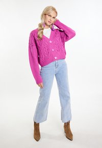 Ružová pletená cardigan s hlbokým V-výstrihom, textúrovaným vzorom lístia a tromi gombíkmi. Kombinovaný so svetlo modrými rovnými džínsami a hnedými členkovými topánkami.