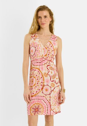 Mujer con vestido sin mangas con escote en V y patrones florales circulares en rosa, naranja y rojo, de pie frente a un fondo blanco liso.