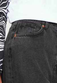 Jeans de mezclilla negros de tiro alto con un acabado texturizado, detalles en metal cobre y un diseño clásico de 5 bolsillos.