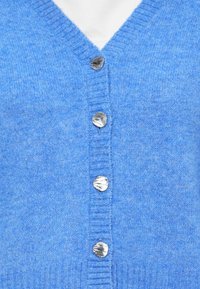 Hellblauer Cardigan aus weicher Wolle, mit V-Ausschnitt, gerippten Bündchen und sechs silberfarbenen, muschelförmigen Knöpfen auf der Vorderseite.