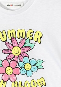 Gyermek fehér pólója vidám, színes mosolygó virágokkal és sárga, vastag betűkkel írt "NYÁR A VIRÁGBAN" felirattal.