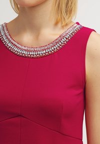 Fuchsia Kleid mit rundem Ausschnitt, ausgestattet mit einem mit klaren Strasssteinen verzierten, beaded Kragen und einer glatten, matten Stofftextur.