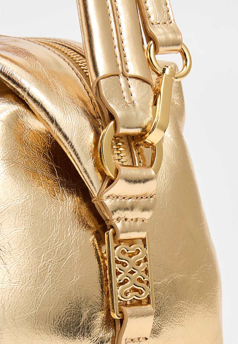 Gouden metallic handtas met een gestructureerd oppervlak, een verstelbare schouderband en decoratieve hardware met een patroonaccent op de gesp.