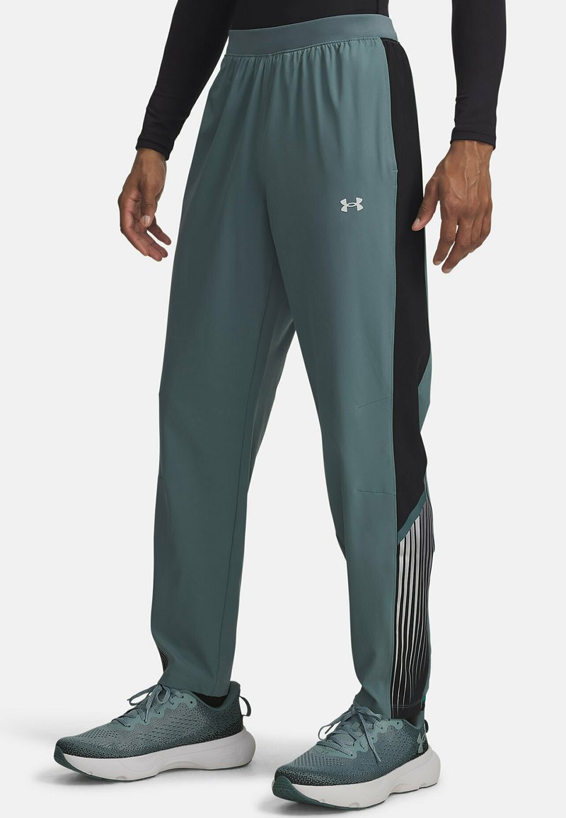 Sportieve broek in teal met zwarte zijkanten. Heeft een lichte, gladde textuur en een gestreept detail langs het onderbeen.
