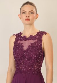 Lila Kleid mit floralem Spitzenstickerei und Perlenakzenten entlang des Ausschnitts, entworfen mit einem taillierten Oberteil und einem fließenden Rock.