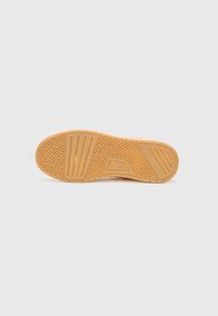 Rubber shoe sole in light tan with textured zigzag pattern and horizontal grooves for traction. Flat with rounded edges, no additional details.