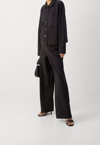 Czarny garnitur w paski zawierający kurtkę z kołnierzykiem, z guzikami z przodu i kieszenią, połączony z szerokimi spodniami i czarnymi sandałkami na obcasie.