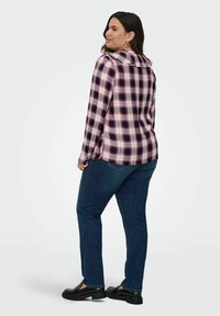 Camicia a maniche lunghe a quadri nei colori blu navy, rosso e bianco, con colletto e dettagli sui bottoni, abbinata a jeans skinny blu scuro e mocassini neri.