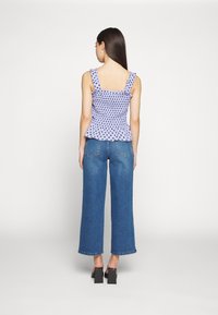 Top roxo com bolinhas brancas, alças com babados, textura franzida e bainha peplum; combinado com jeans azuis de perna larga e sapatos de salto bloco.