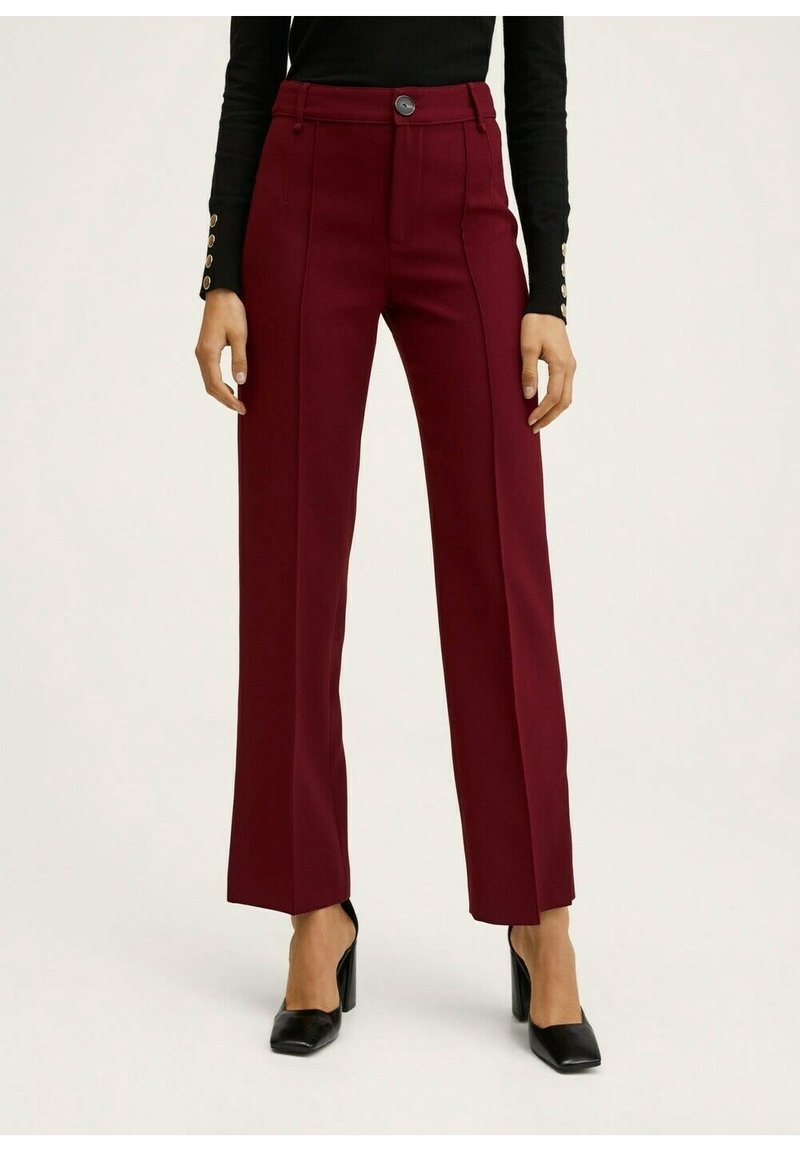 Femme portant un pantalon bordeaux taille haute à jambes droites avec un bouton noir, associé à un haut noir à manches longues et des talons noirs.