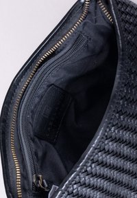 Black woven leather bag interior, featuring a zip pocket and a black fabric lining with a label. Gold zipper hardware detail visible.