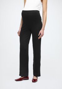 Schwarze Umstandshosen mit elastischem Bund, geradem Bein, weicher Textur, kombiniert mit glänzenden roten Ballerinas.