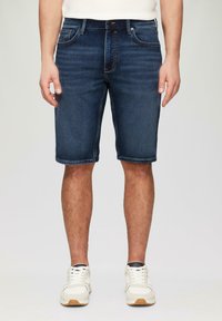 Donkerblauwe denim shorts met een standaard vijf-pocket ontwerp, rechte pijpen en zichtbare stiksels langs de zoom. Witte sneakers maken de look compleet.