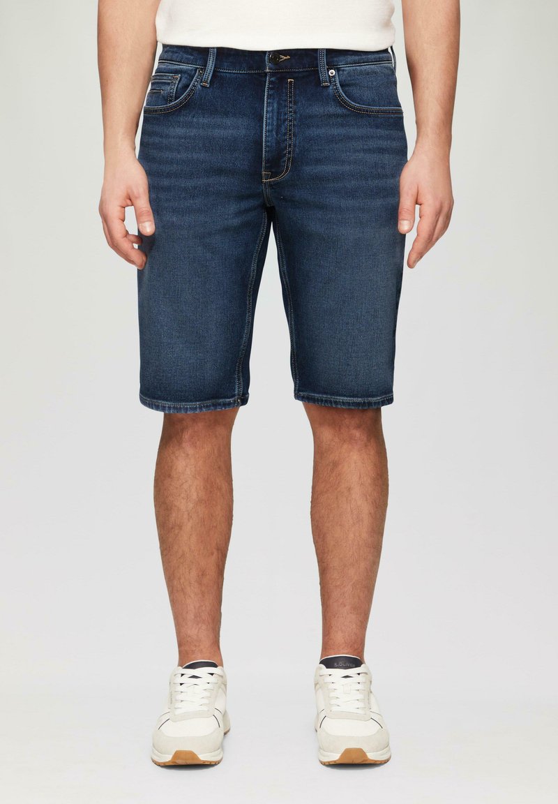 Donkerblauwe denim shorts met een standaard vijf-pocket ontwerp, rechte pijpen en zichtbare stiksels langs de zoom. Witte sneakers maken de look compleet.