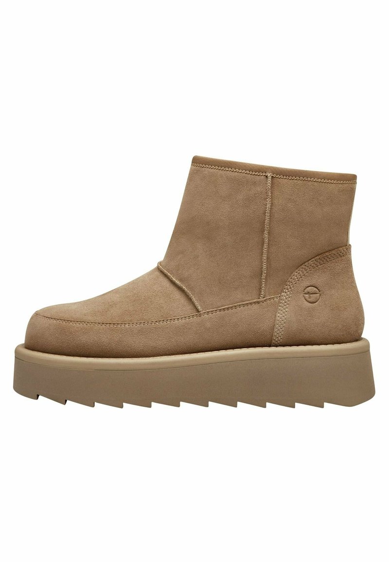 Bottines en daim beige avec une finition lisse, un bout arrondi et une semelle épaisse et plate en caoutchouc. Détails de coutures et logo sur le côté.
