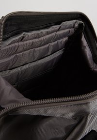 Černá látková taška uvnitř s několika šedými přihrádkami, texturovaným podšívkou a zipem na otevírání. Obsahuje polstrované sekce pro ochranu.