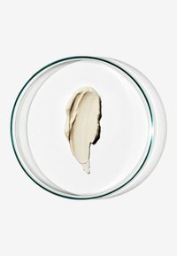 Beige roomkleur textuur uitgespreid op een witte ondergrond, in een transparante glazen schaal. Gladde consistentie met een subtiele glans en zachte randen.