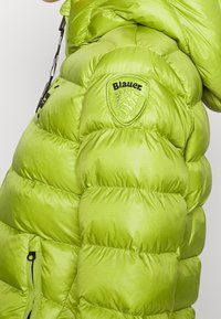 Limegrøn pufjakke med en blank finish, der har kviltede sektioner, et logo patch og lynlås lommer foran.