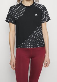Camiseta deportiva negra con mangas cortas estampadas con triángulos blancos, acompañada de mallas color granate.