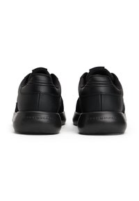 Le scarpe da ginnastica nere presentano una tomaia in pelle e tessuto liscia con suole in gomma. Il design include un branding minimale sul tallone.