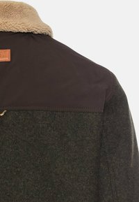 Wool jacket featuring a brown, fur-lined collar, rich green body, and a leather label. The collar has a smooth, contrasting texture.