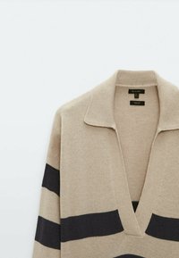 Beige trui met diepe V-hals, korte kraag en zwarte horizontale strepen. Gemaakt van zacht gebreide stof met een gladde textuur.