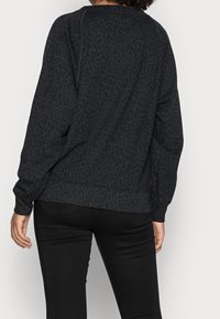 Sweat-shirt noir avec un imprimé léopard subtil, manches longues et encolure ronde, associé à un pantalon noir. Texture douce et coupe décontractée.