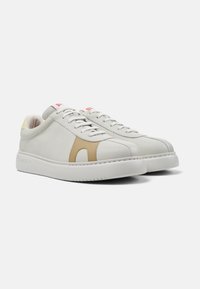 White sneakers with a smooth leather upper, beige accents, pink branding, and a yellow heel tab, featuring a rounded toe and chunky sole.
