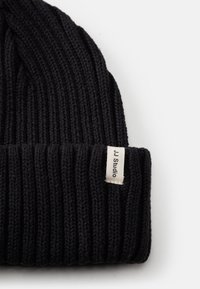 Mustmustri mustriga beanie, millel on sooniline tekstuur, volditud ääre ja külje peal väike valge silt, millel on kirjutatud "JJ Studio".