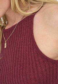 Haut sans manches en tricot côtelé bordeaux avec un col rond, présentant un tissu texturé et un collier en chaîne dorée fine avec un pendentif rectangulaire.