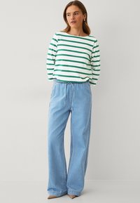 Wit en groen gestreepte lange mouw top gecombineerd met lichtblauwe wijde broek met een trekkoord in de taille en een zachte denim textuur.
