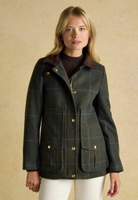 Giacca di lana a quadri verdi con colletto marrone, accessori dorati e due tasche frontali. Presenta un design aderente e un tessuto testurizzato.