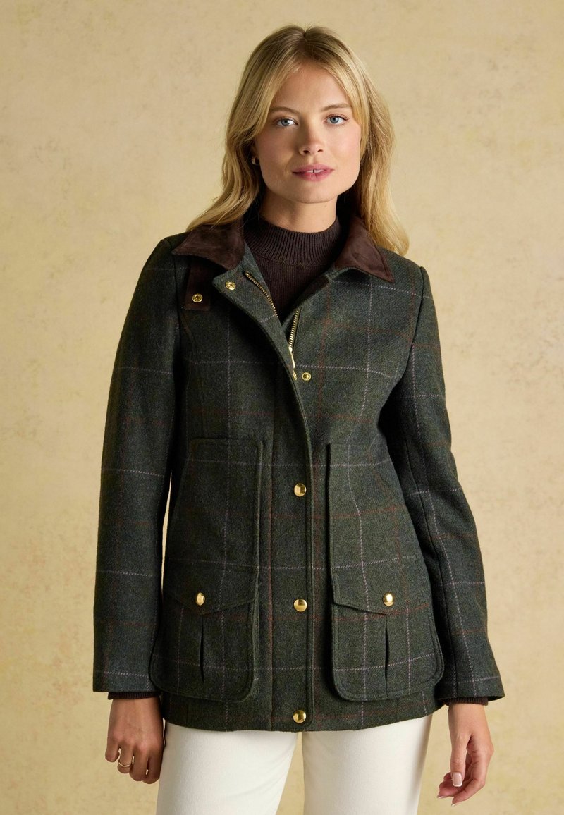 Giacca di lana a quadri verdi con colletto marrone, accessori dorati e due tasche frontali. Presenta un design aderente e un tessuto testurizzato.